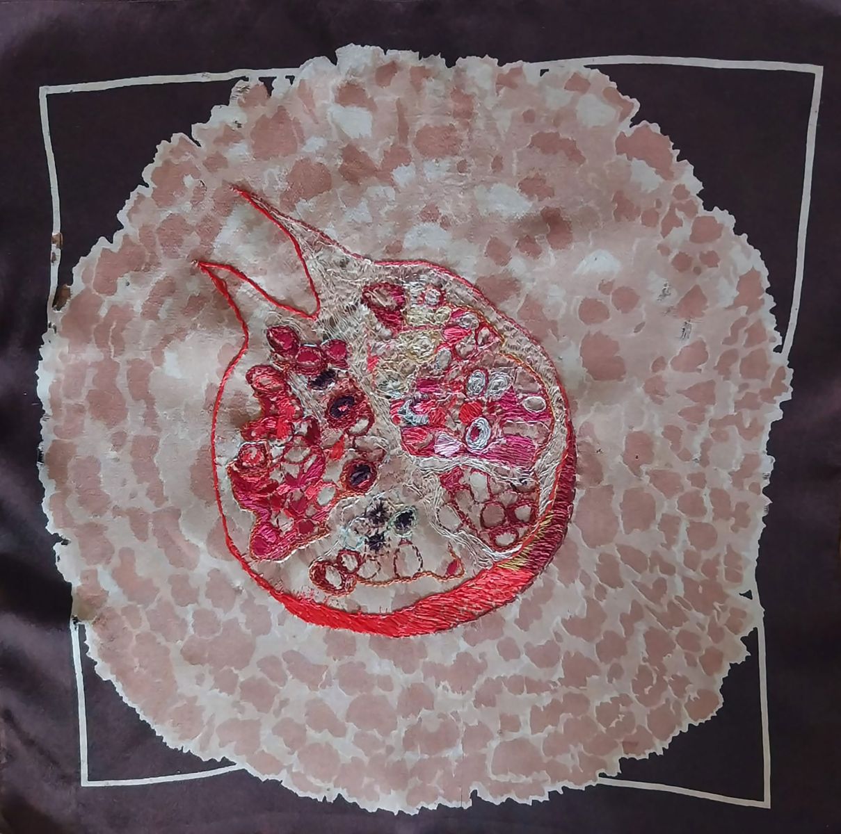 pink embroidery on black background, showing schematic representation of the cross-section of a pomegranate, with seeds inside