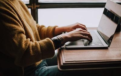 Image shows a female in a yellow jumper sitting at a desk and typing on a laptop. Photo credit Christin Hume, Unsplash