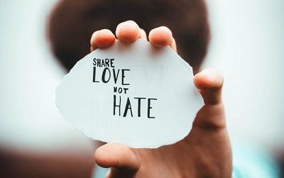 Image shows a hand holding a note up close to the camera which says "Share Love Not Hate". Photo credit: Dan Edge on Unsplash
