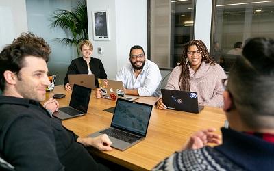 A team sit around a table with laptops in a meeting. They look happy