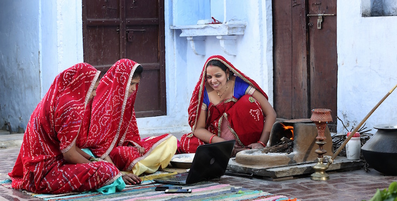 Photo of three women wearing identical saris gathered round a laptop
