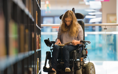 A woman in a wheelchair reading a book in a library.