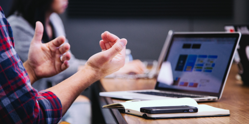 Someone talking with their hands at a desk in front of a computer