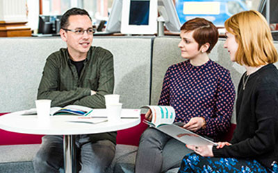 three people sit at a table having a conversation