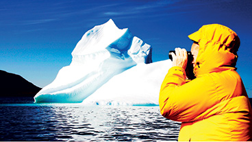 Someone looking through binoculars with an Iceberg in the distance.