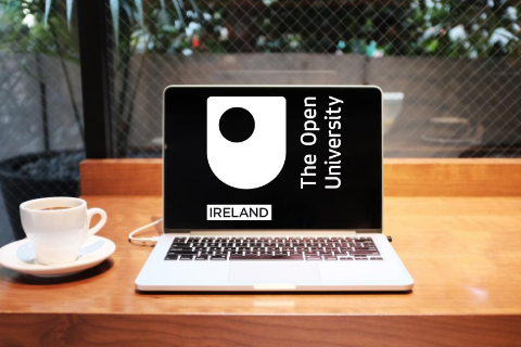 A laptop with the OU in Ireland logo and a cup of coffee on a desk