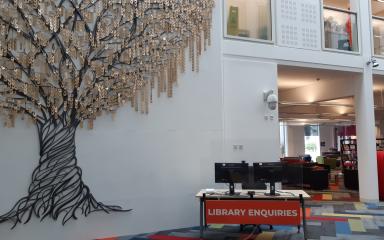 A photo of the Enquiries desk on the ground floor of the Library building, positioned next to the Tree of Learning.