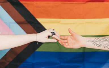 hands reaching across LGBTQ+ flag