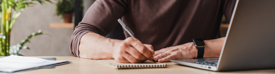 Student making notes while working from a laptop