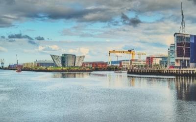 An exterior shot of Belfast showing the Titanic Museum and Harland and Wolff cranes from across the river
