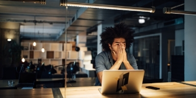 A man sitting at a desk with hands over his face looking worried in front of a laptop