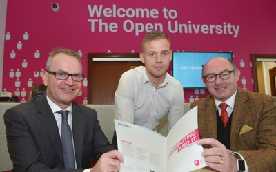 three men pose for a photo and two fold a prospectus between them