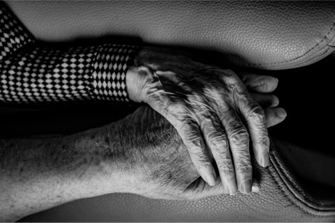 A black and white landscape photo of two elderly hands resting on one another 