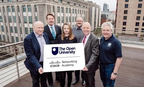 A group of people posing for a photo holding a prop which has the OU logo and the Cisco Networking Academy logo