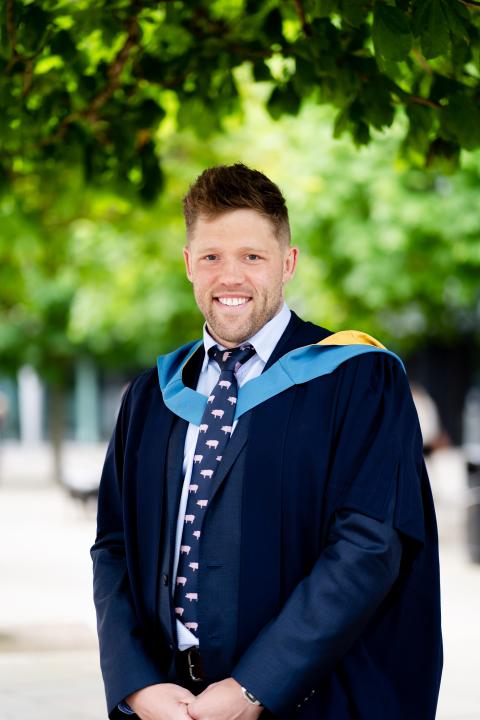 Jonny, stood outside smiling wearing his Open University degree robes.