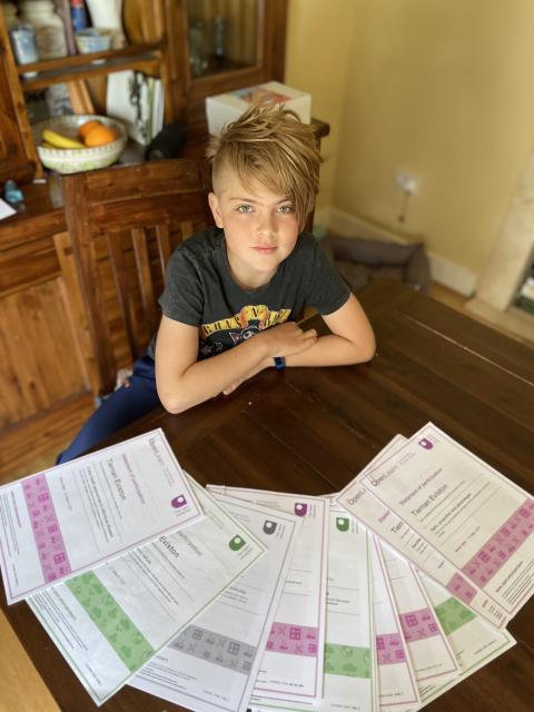 A young boy sitting at the kitchen table with his certificates spread out in front of him