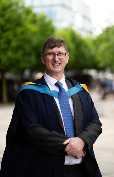 William photographed in his graduation gown, he is smiling and wearing glasses