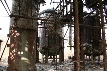 An image of a decaying structure, with two rusty tanks and many rusty pipes.