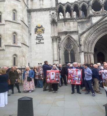 Protesters are shown, some holding placards, outside the Royal Courts of Justice