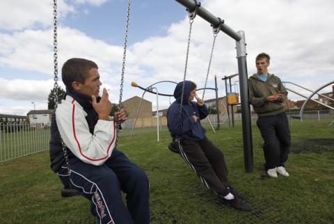 Three young people on swings in a park.