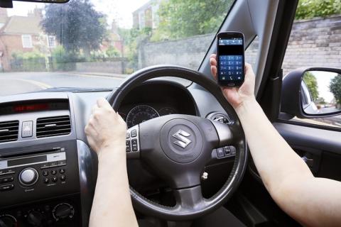 A person using their mobile phone at the wheel of a car.