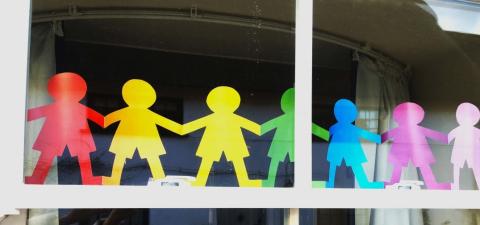 Paper cutout of people in rainbow colours holding hands.