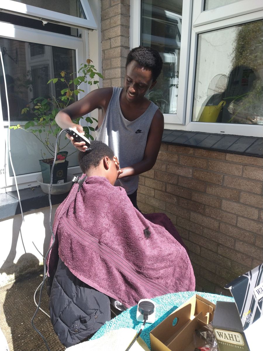 A male cuts the hair of a younger male outside