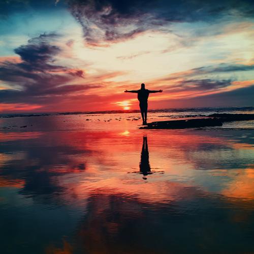man standing with open arms in the sunset