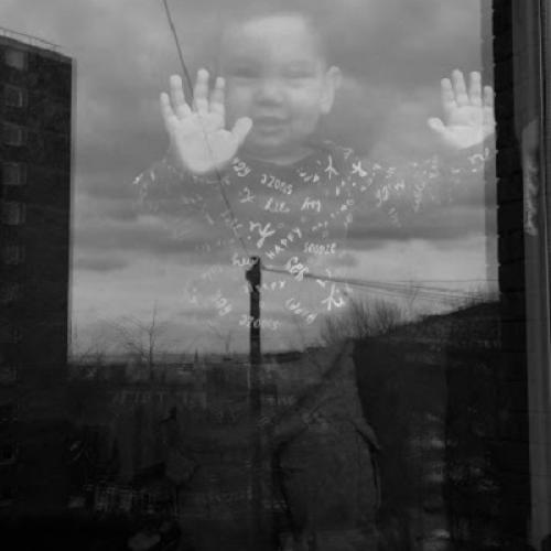 A gorgeous, happy toddler stands with his hands pressed up against a window smiling at the refugee art photographer