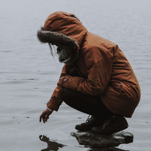 women wearing winter coat kneel near the water