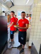 Two men stand in a catering establishment in red shirts