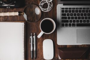 Laptop, coffee, pens, notebook, magnifying glass on a table