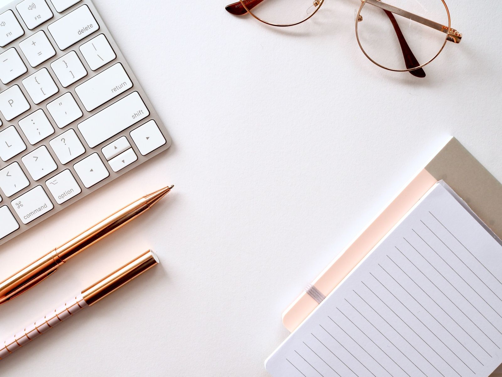 Notebook, keyboard, pen, and glasses on a desk