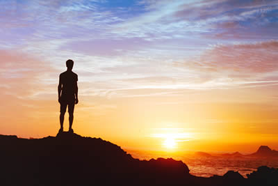 Man standing on a mountain looking out over a beautiful sun rise and landscape