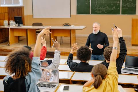 A picture of a university lecture hall. Students are participating in the lecture by raising their hands.