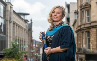 OU graduate Carol, standing in her gown outside the Glasgow Royal Concert Hall on graduation day