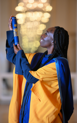 Eunice Olumide wearing OU honorary graduate robes and holding a graduation scroll. 