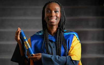 Eunice Olumide wearing OU honorary graduate robes and holding a graduation scroll. 