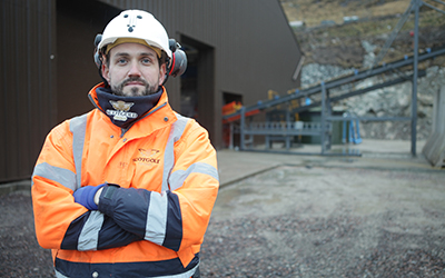 A man wearing a hard hat and in an orange Scotgold jacket, outside a Highlands mine 