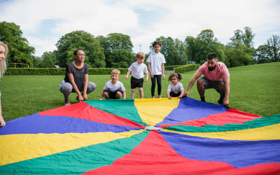 Adults and young children pictured outdoors with a parachute