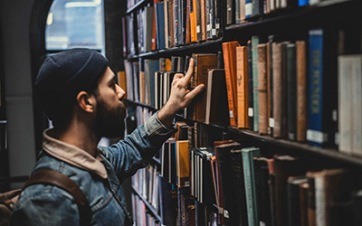 A male student looking at books on library shelves