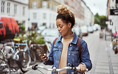 A young woman on a stationary bike, looking at her mobile phone 