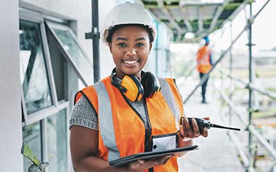 A female construction site worker, holding a digital tablet and walkie talkie