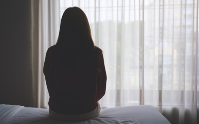 Photo posed by model, from iStock. A silhouette of a woman (back to camera) sitting on the edge of a bed.