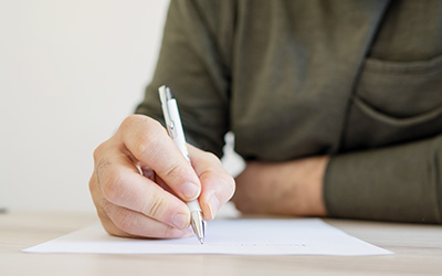 A close up image of a hand holding a pen, poised to write on a sheet of paper