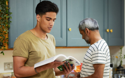 A man studying in the kitchen whilst his family are cooking behind him