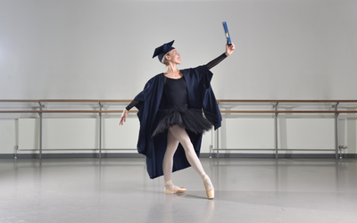 Principal dancer Constance Devernay-Laurence in a graduation gown, holding an OU degree scroll, at Scottish Ballet's studio. Photo by Julie Howden. 