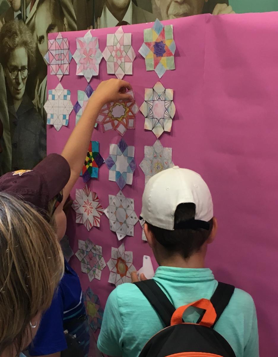 Children posting mathematical designs to a poster board